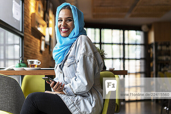 Young woman wearing turquoise hijab and using smartphone in a cafe