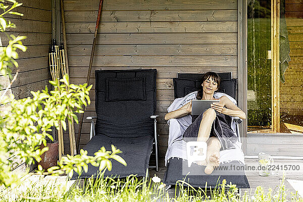 Woman relaxing on a lounge outside sauna using tablet