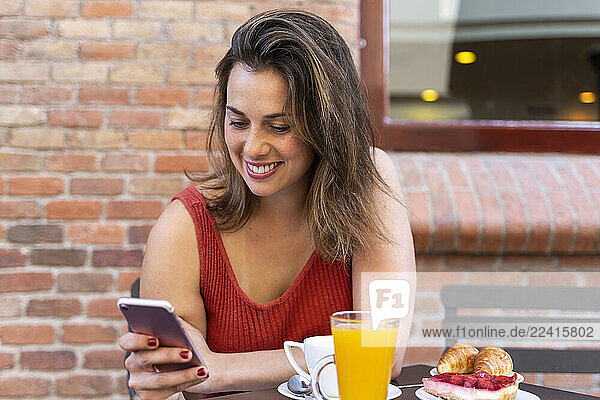 Smiling young woman sitting at street cafe looking at cell phone
