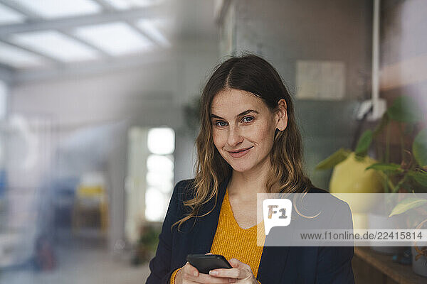 Businesswoman using smartphone in office smiling at camera