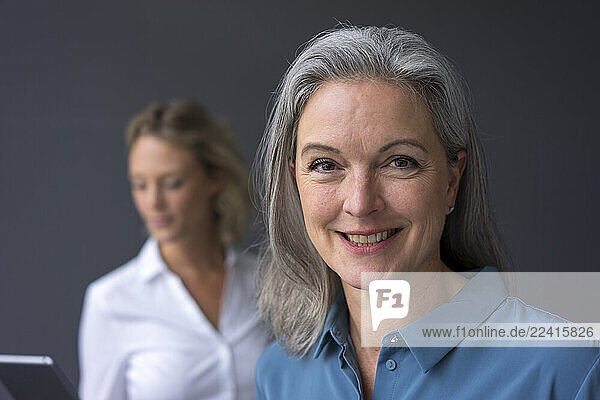 Portrait of smiling mature businesswoman with young businesswoman in background