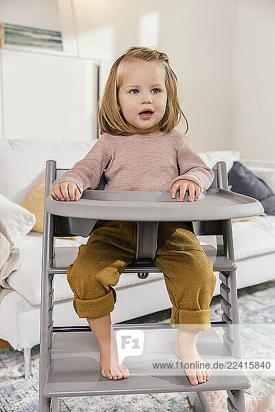 Little girl sitting on high chair at home