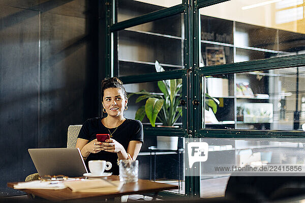 Casual young businesswoman with laptop and smartphone in loft office