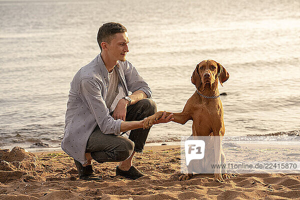 young man with his dog at the beach  dog giving paw