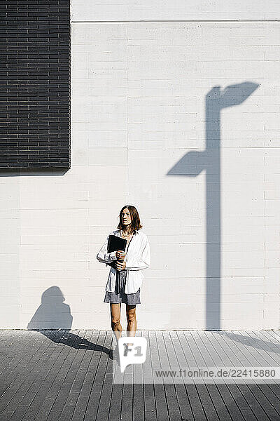 Pretty woman standing in front of building  carrying folder