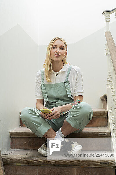 Portrait of young woman sitting in staircase with cell phone