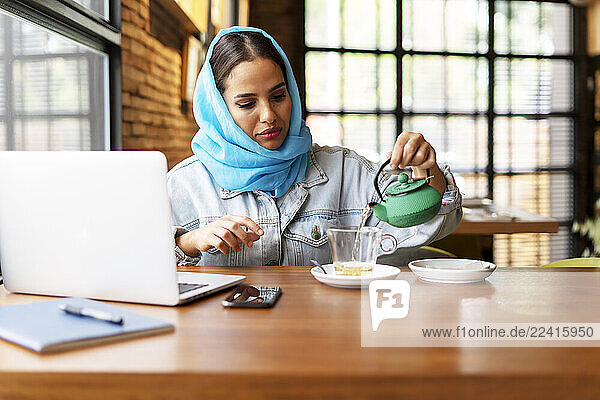 Businesswoman wearing turquoise hijab in a cafe and working  pouring tea