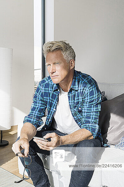Casual businessman sitting in modern home holding smartphone