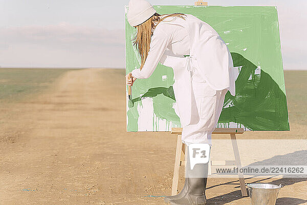 Young woman on dry field  painting canvas with green paint