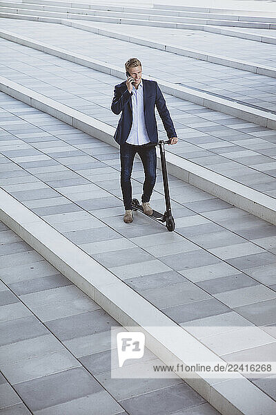 Young man with e-scooter talking on the phone on a city square
