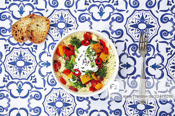 Bowl of couscous with grilled vegetables and yoghurt sauce on patterned tablecloth