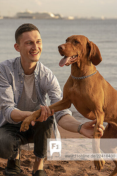Young man with his dog at the beach  dog giving paw