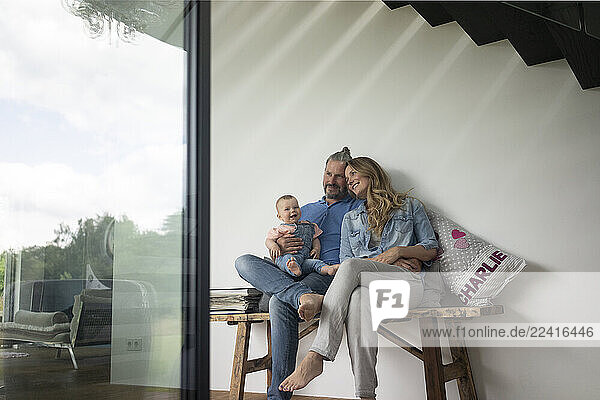 Happy family of three sitting on a bench at home