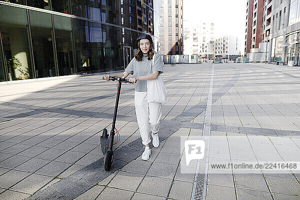 Woman with e-scooter and helmet  modern office buildings in the background