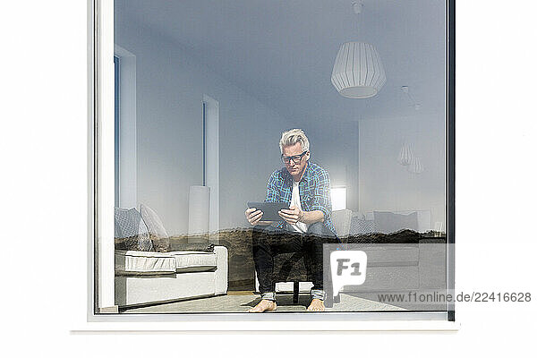 Casual businessman sitting in modern home looking at tablet