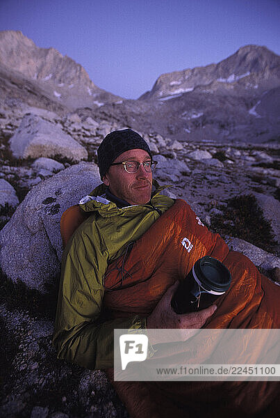 Man in his sleeping bag with a hot drink in Eastern Sierra Nevada mountains  California.