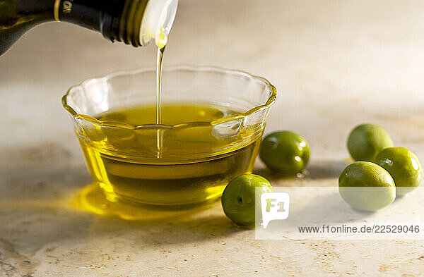 Olive oil pouring into small glass bowl with olives on table