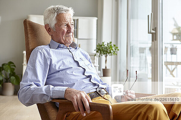 Senior man sitting in an armchair at home  looking thoughtful and content.