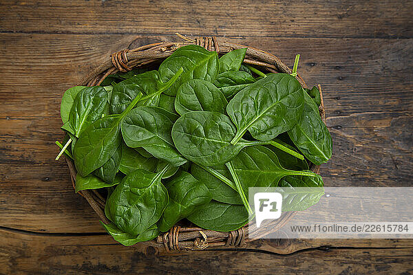 Fresh baby spinach in a willow basket on a wooden background