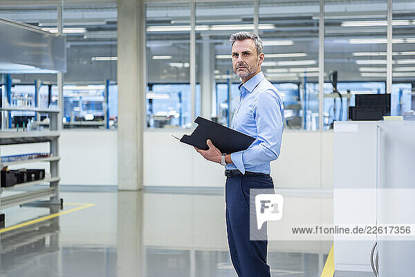 Business professional in a production hall holding a clipboard