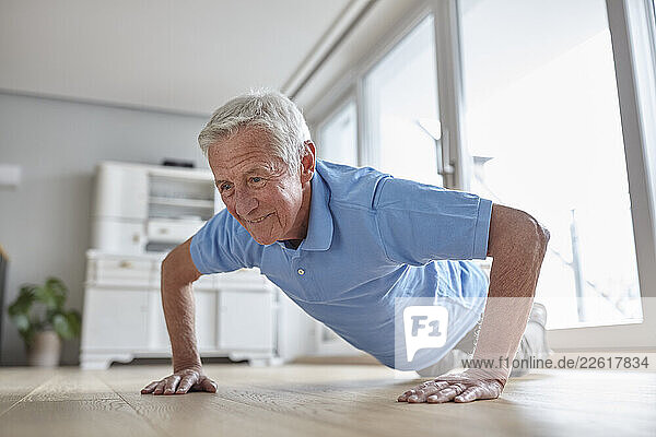 Senior man doing push-ups indoors with a smile