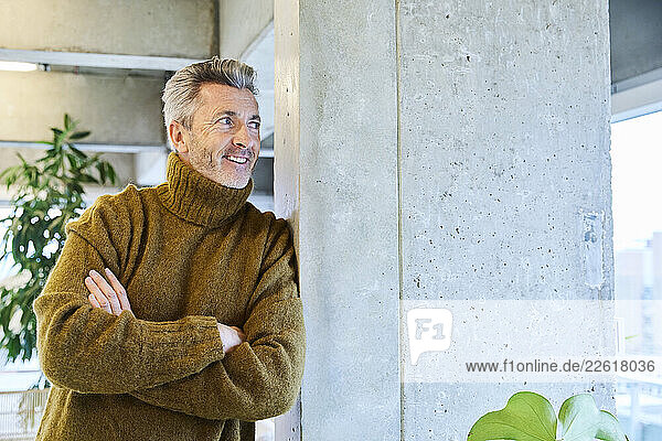 Man with arms crossed looking away while leaning on pillar at office