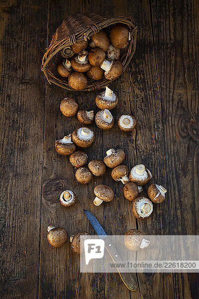 Brown mushrooms spilling from a willow basket onto a wooden table with a knife.