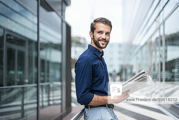 Confident businessman holding a newspaper outdoors in a modern urban setting