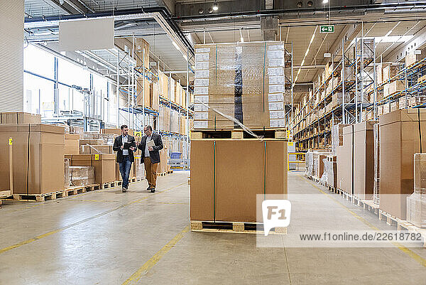 Employees meeting in a large warehouse with stacked pallets and boxes