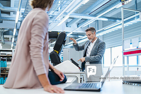 Man and woman discussing in a production hall with an industrial robot