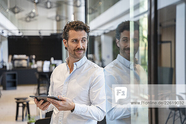 Young man in an office holding a tablet and looking away with a smile