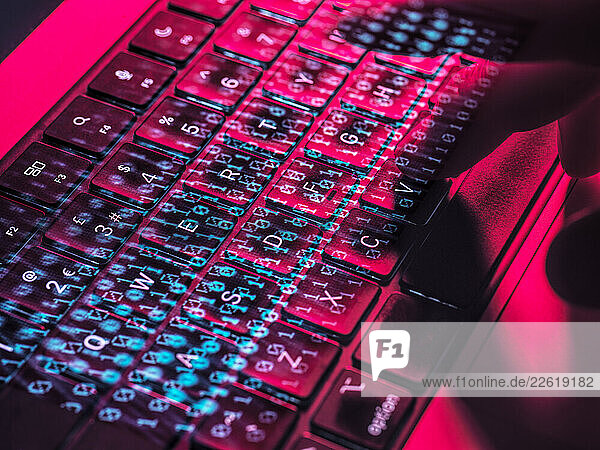 Close-up of a hand typing on a laptop keyboard with neon lighting  representing cybersecurity and cyber crime concepts