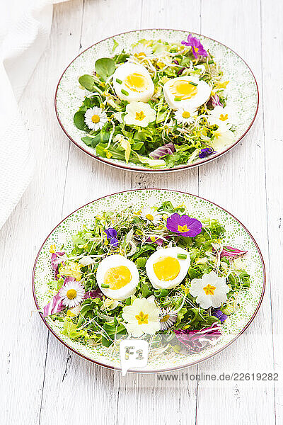 Spring salad with hard boiled eggs and edible flowers on a wooden table