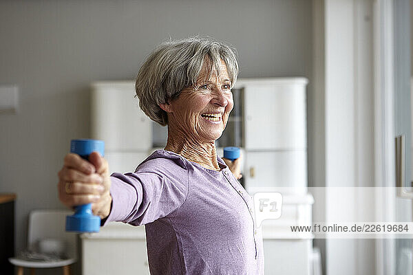 Smiling woman exercising with dumbbells indoors
