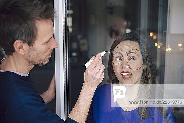 Couple having fun drawing glasses on a window at home