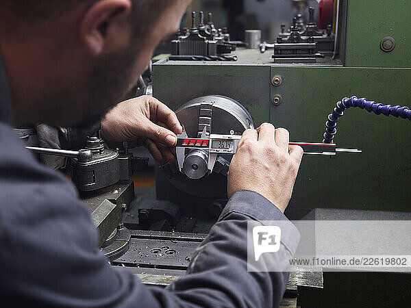 Metal construction technician measuring with calipers at a lathe in a workshop