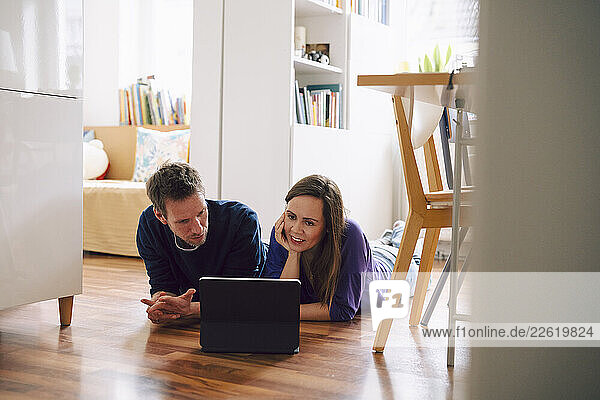 Couple lying on the floor at home using a tablet for communication