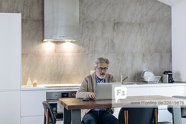 Mature man using laptop at table in kitchen at home