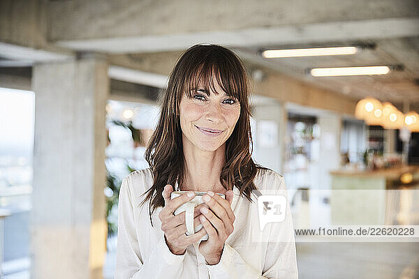 Smiling mature woman holding coffee cup while standing at home