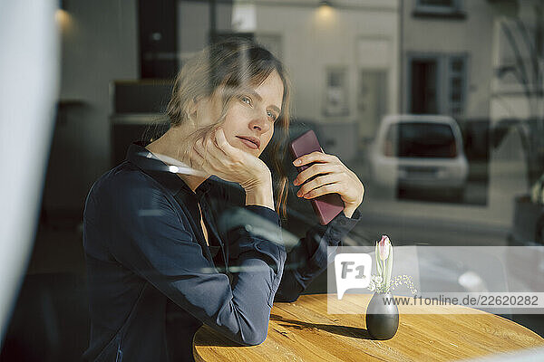 Woman in a café contemplating through a window with a smartphone