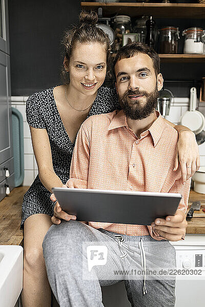 Young couple sitting on kitchen worktop  using digital tablet