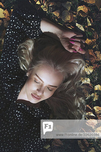 Blond woman relaxing on autumn leaves in a park