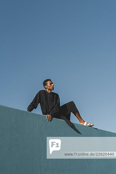 Young man wearing black kaftan on blue wall