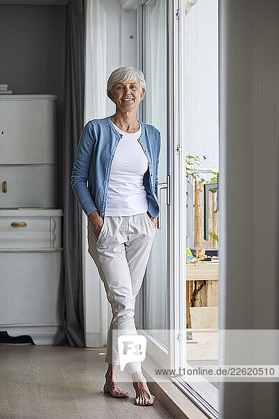 Smiling woman standing barefoot by a window at home