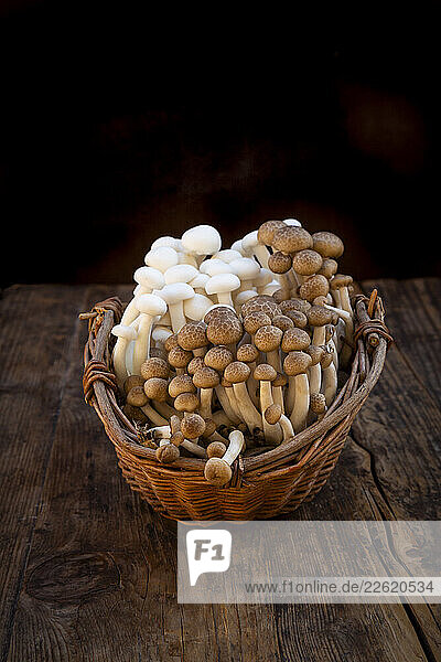 White and brown beech mushrooms in a willow basket on a wooden table