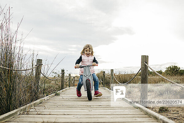 Toddler girl with balance bicycle on a boardwalk in the countryside