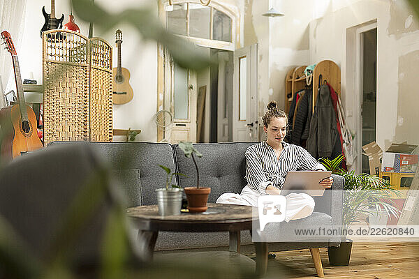 Young woman sitting ob couch  holding digital tabet