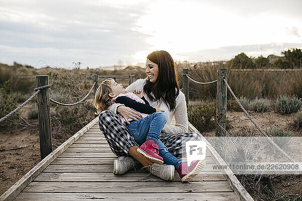 Happy mother and daughter sitting on a boardwalk in the countryside