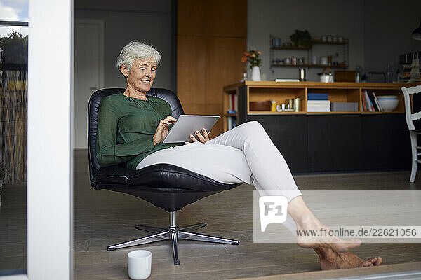 Woman relaxing at home using a tablet in a modern chair