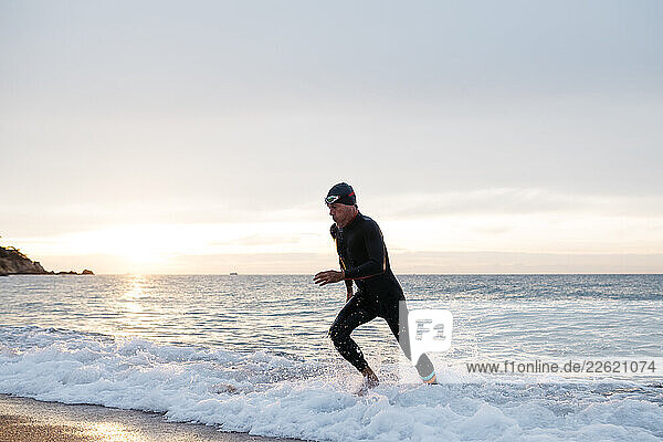 Male swimmer leaving water after swimming in sea at sunset